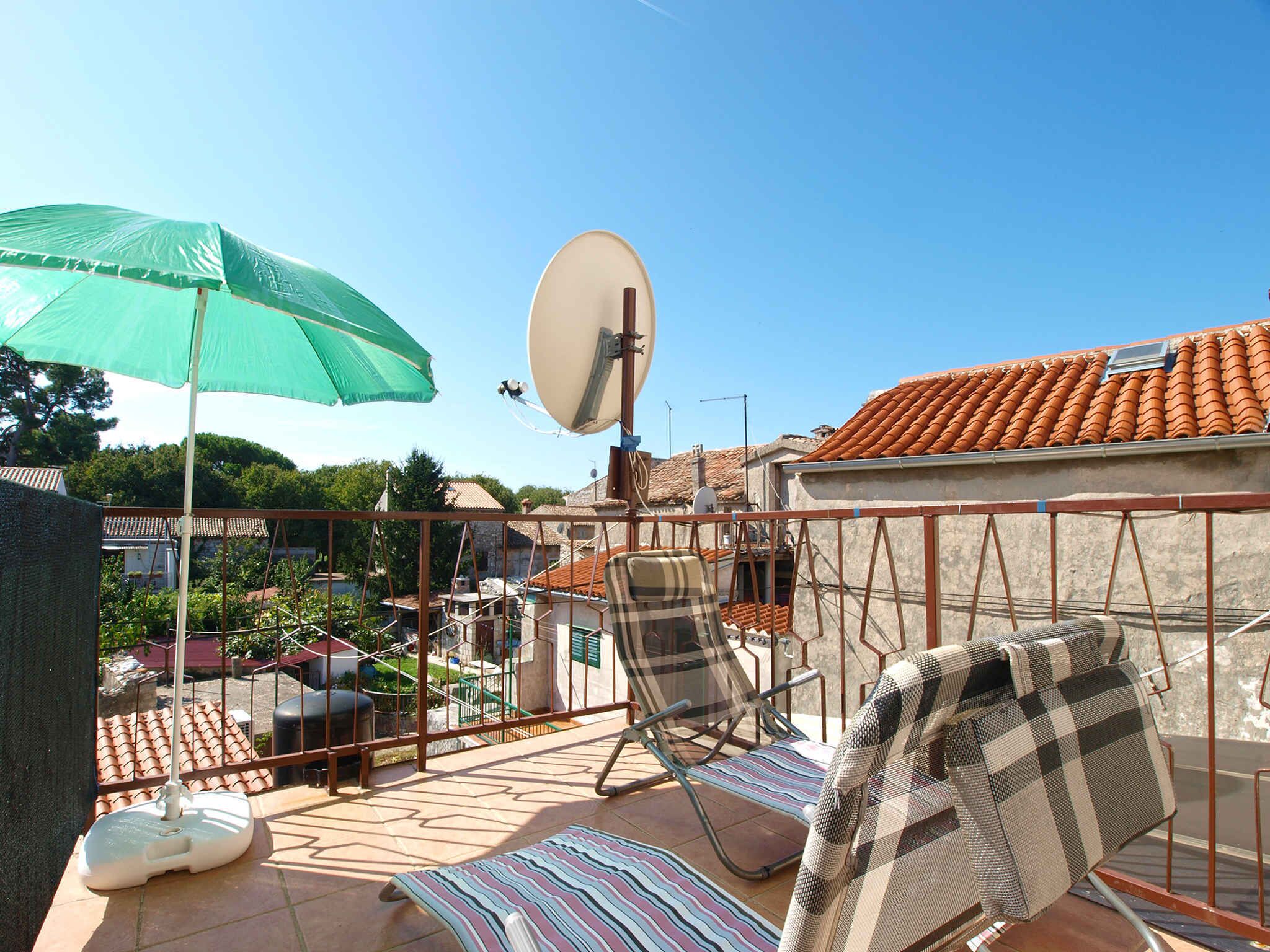 Une terrasse sur le toit, avec une antenne parabolique, un parasol vert et des chaises longues.
