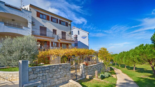 A multi-story residential building with balconies, a stone wall, and a pathway leading to the entrance.