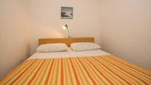 A single bed with a striped bedspread, a wooden headboard, two pillows, a bedside lamp, and a small picture on the wall. - Holiday apartment with air conditioning (Pješćana Uvala)