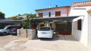 A white car parked in a covered garage area with a stone wall and potted plants. - Holiday apartment with air conditioning (Pješćana Uvala)