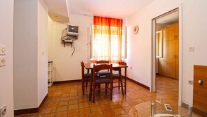 A dining area with a table and chairs, a television mounted on the wall, and a window with curtains. - Holiday apartment with air conditioning (Pješćana Uvala)