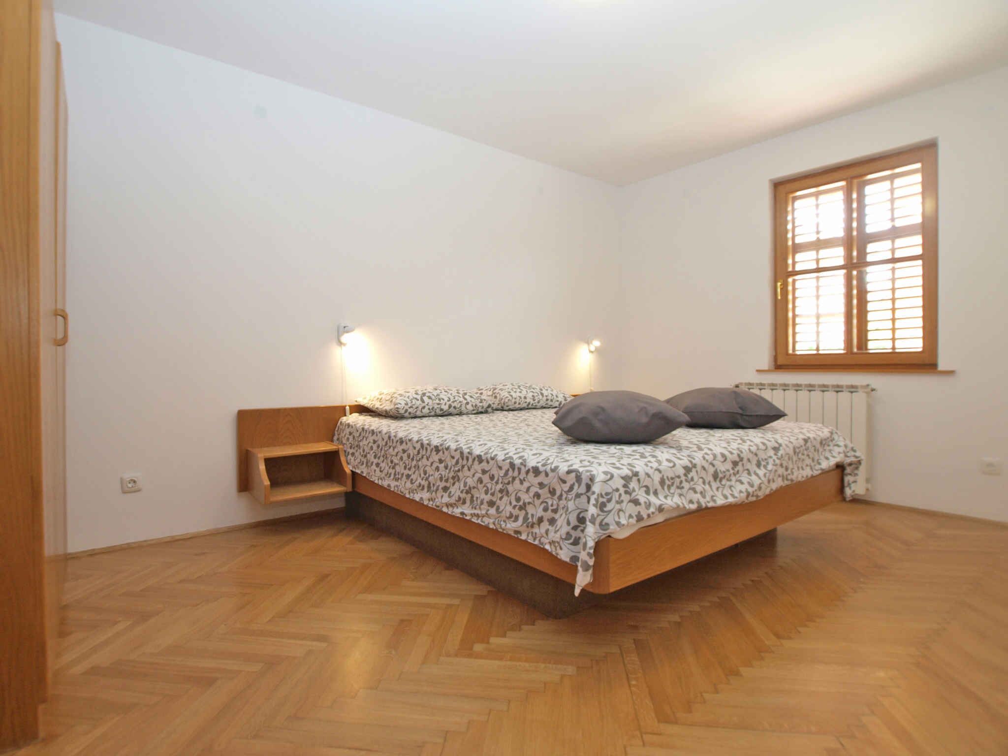 A bedroom with a bed, two bedside lamps, a window, and a radiator.