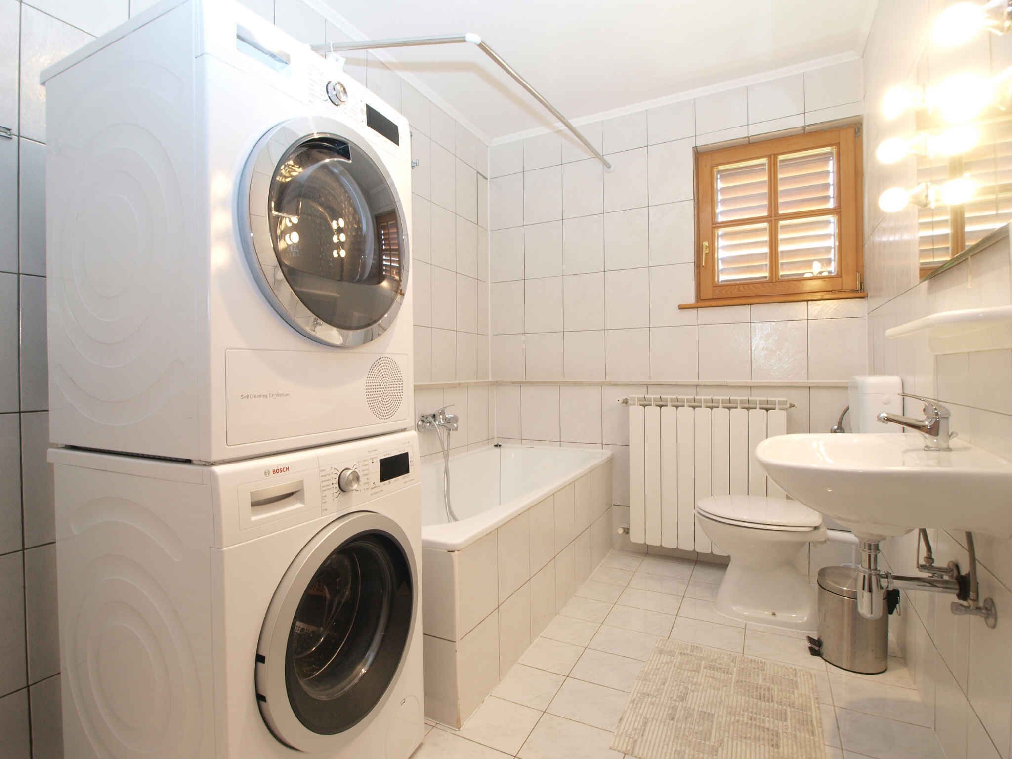 Ein modernes Badezimmer mit einer Waschmaschine von Bosch, einer Badewanne, einer Toilette und einem Waschbecken.