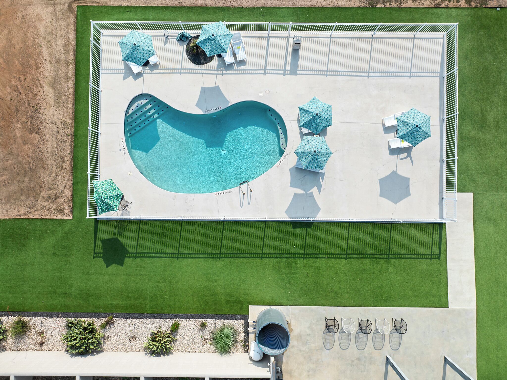 Vista aerea di una piscina dalla forma particolare, circondata da un solarium con ombrelloni e lettini.