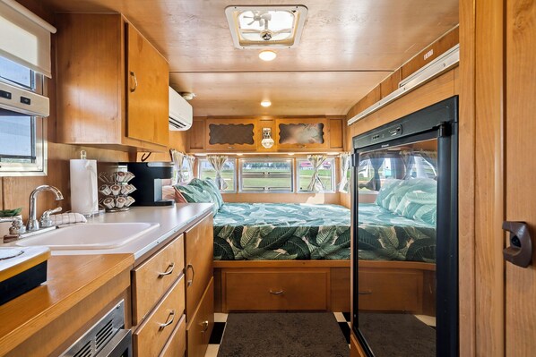 Eine kleine Küchenzeile in einem Wohnmobil mit Holzausbau, Spüle und Kühlschrank.