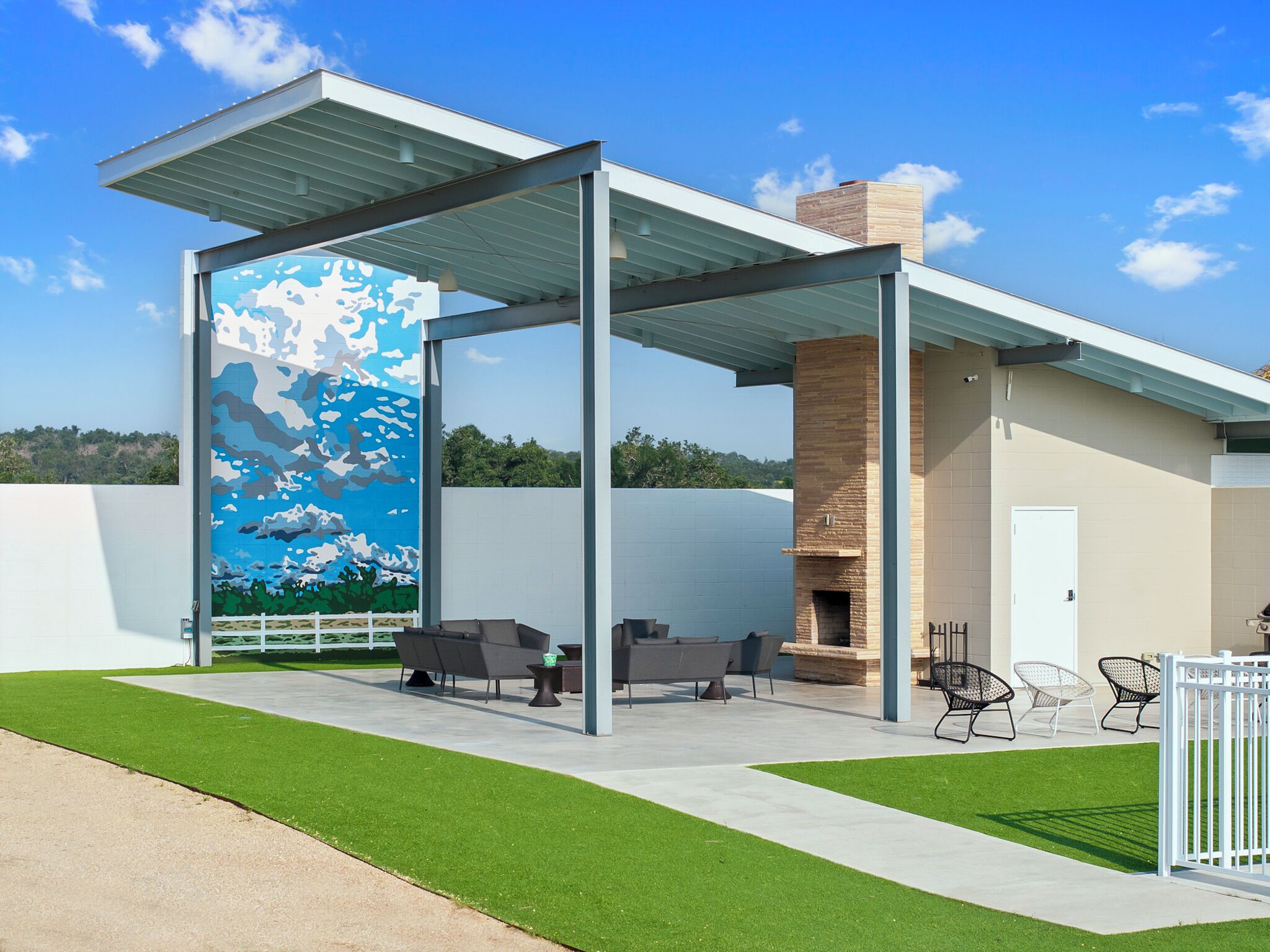A modern outdoor patio with a mural, outdoor seating, and a brick fireplace.