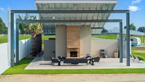 Un espace de détente extérieur moderne, doté d’un foyer, entouré d’une structure en métal et surmont é d’un toit en verre.