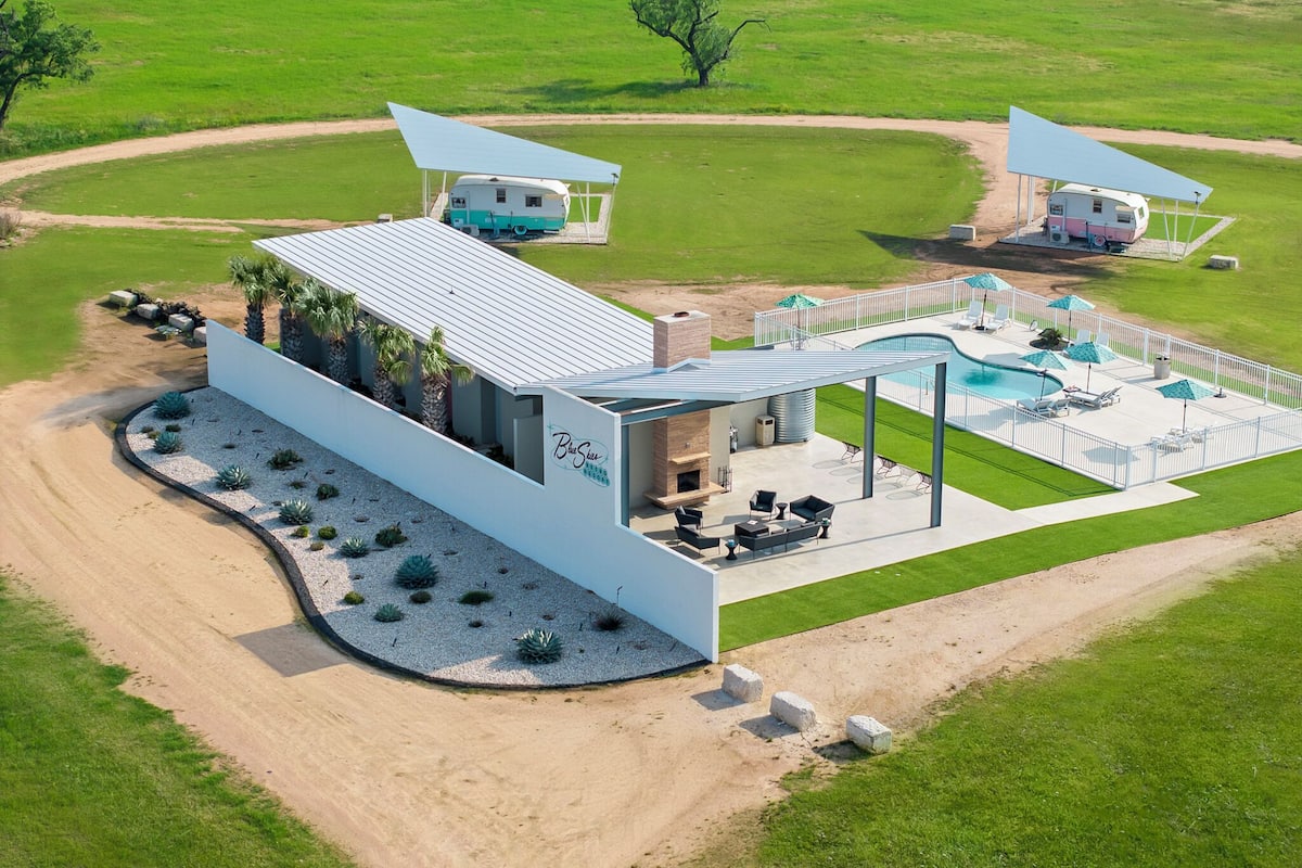 Un moderno resort con piscina, mobiliario exterior y un edificio grande con un porche cubierto.