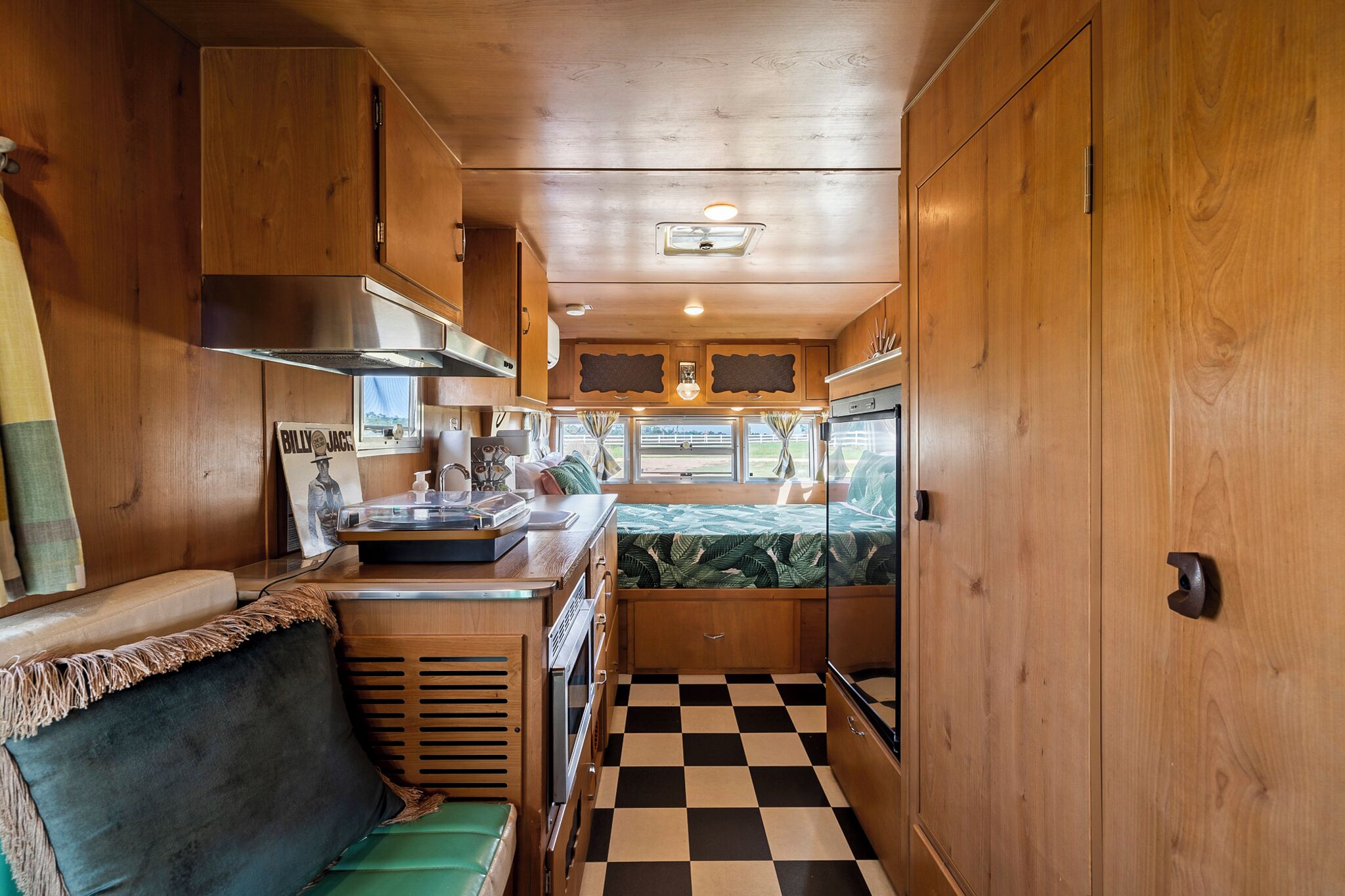 A compact RV kitchen with wooden cabinetry, a checkered floor, and a small seating area.