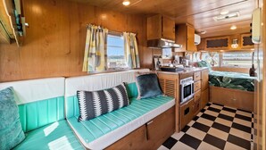 Un intérieur de camping-car compact comprenant un coin cuisine, un espace salon avec des coussins et un sol à carreaux.