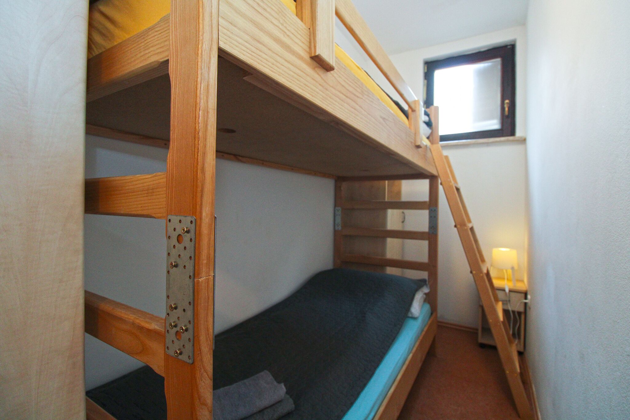 A bunk bed room with a window, a desk with a lamp, and a ladder.
