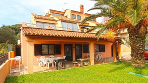 A two-story house with a patio area, outdoor furniture, and a palm tree. - Holiday apartment with air conditioning (Pješćana Uvala)