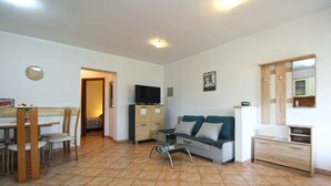 A living room with a sofa, TV, and a dining area with chairs and a table. - Holiday apartment with air conditioning (Pješćana Uvala)