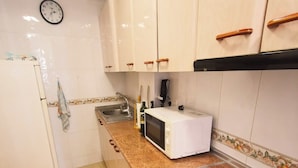 A kitchen with white cabinets, a microwave, a stove, and a clock on the wall. - Centro Cerca Playa (Benidorm)