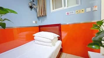 A small, single-bed room with orange and blue walls, a window with curtains, and a wall-mounted sign.