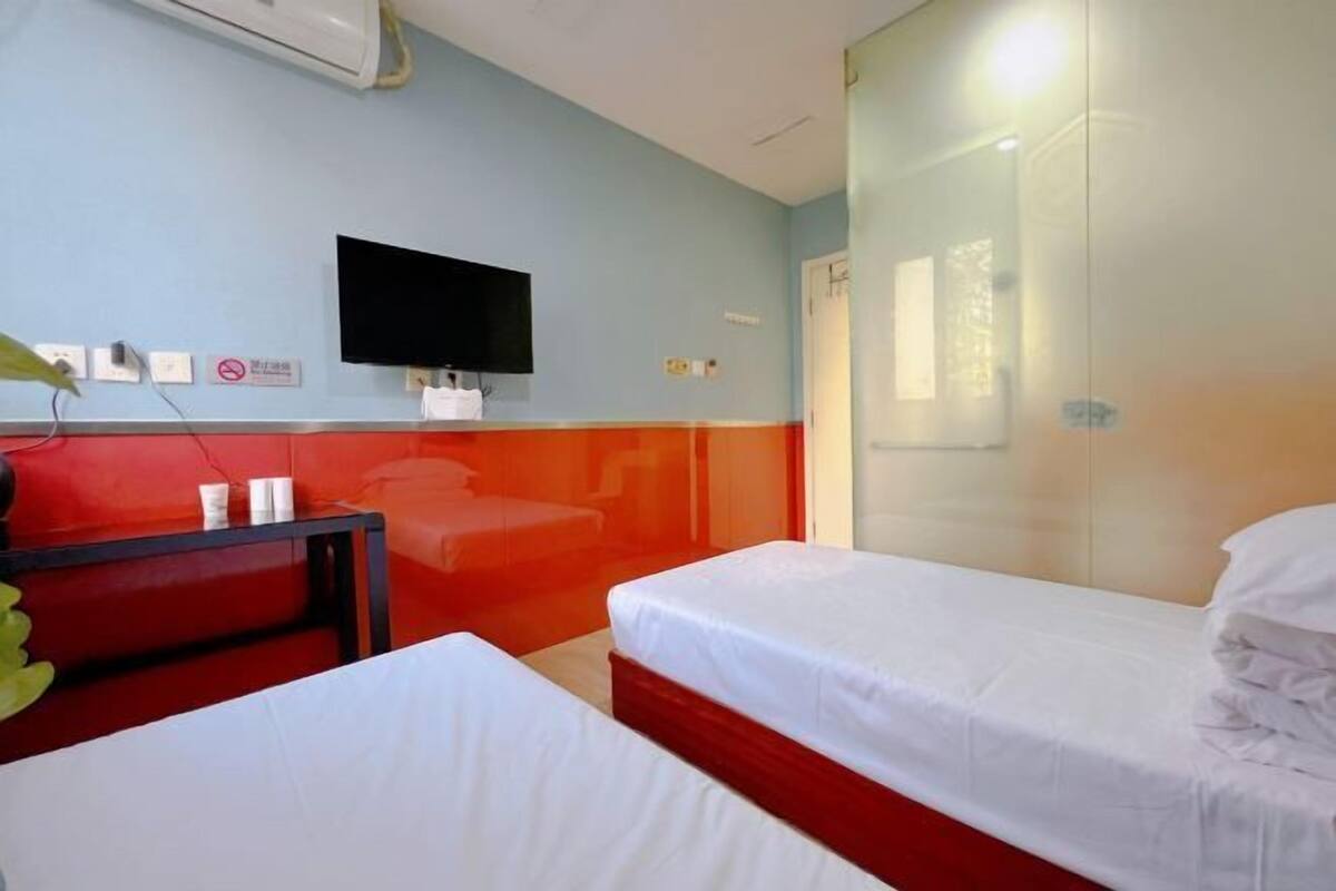 Quarto de hotel com duas camas, uma TV fixada na parede e uma parede de destaque vermelha.