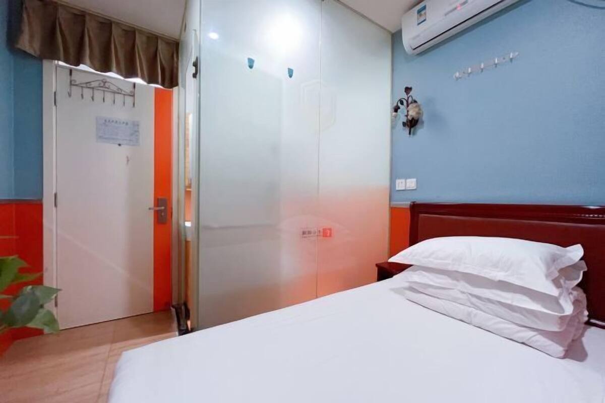 Quarto de hotel com cama, guarda-roupa, ar condicionado fixado na parede e uma porta vermelha.