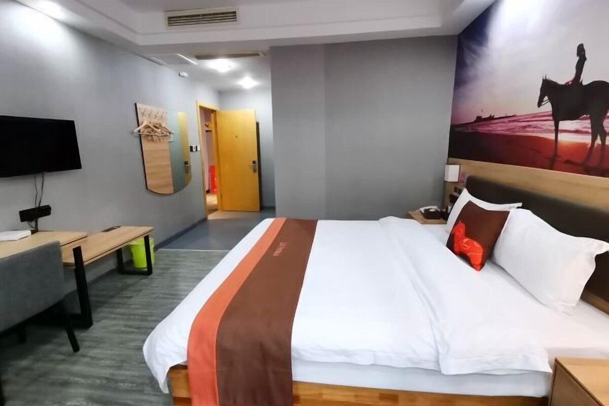 A hotel room with a bed, a desk, a chair, a TV, and a door leading to another room.