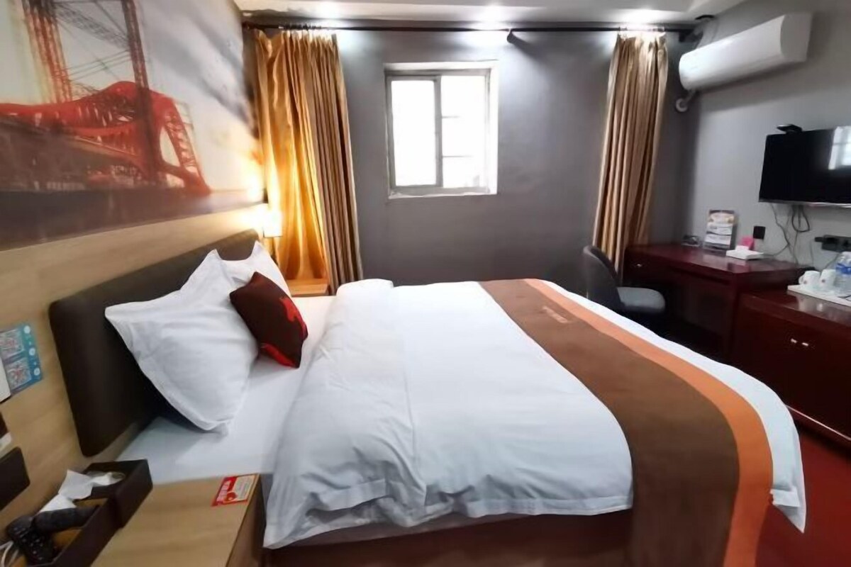 A hotel room with a bed, a desk, a chair, a television, and a window.