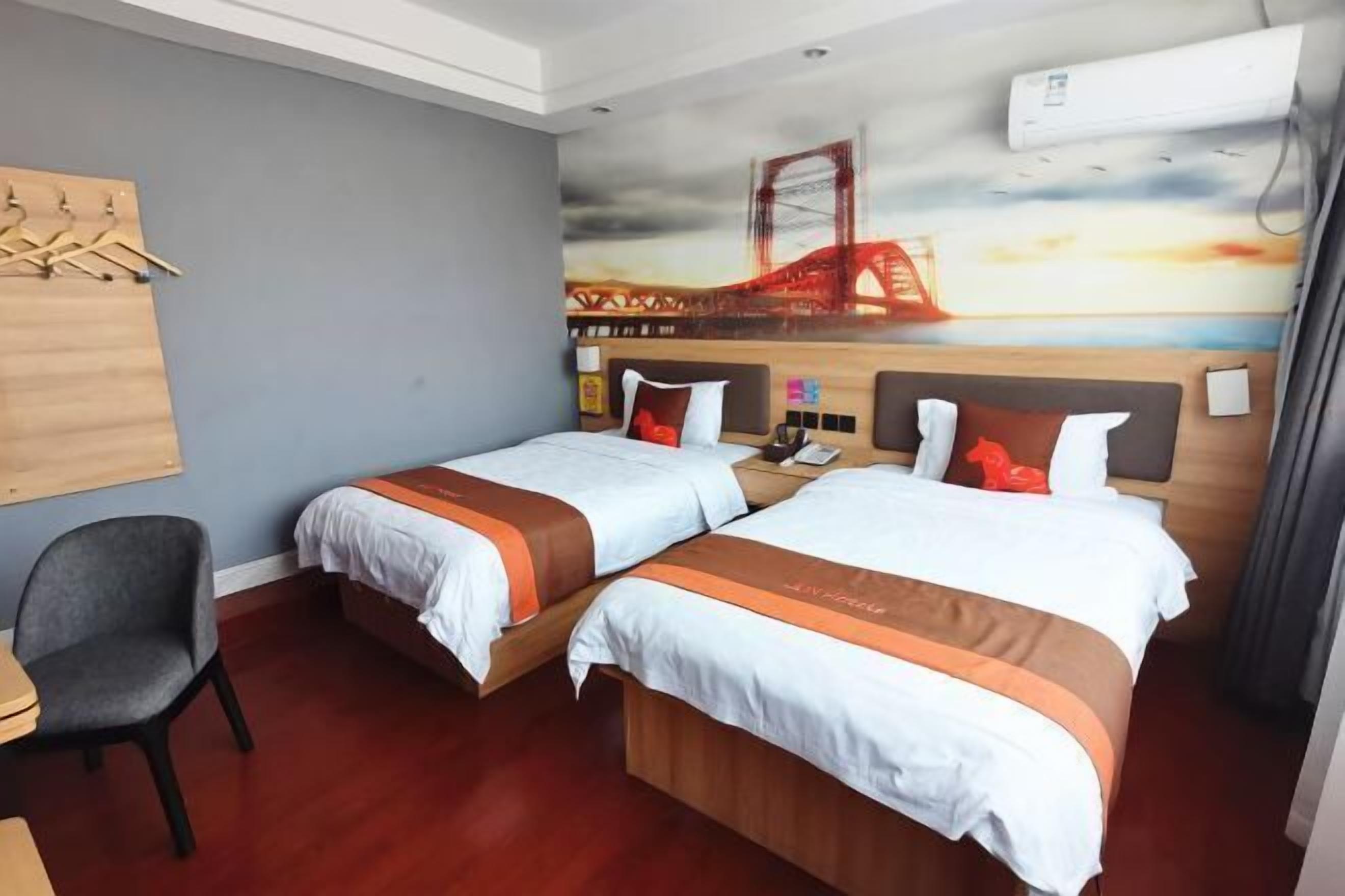 A hotel room with two beds, a desk, and a chair. There is a mural of a bridge on the wall.