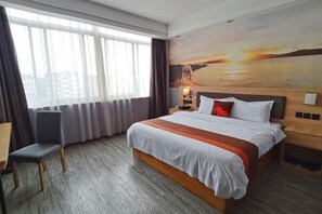A hotel room with a large bed, a desk, a chair, and a view of a sunset through the window. - Junyi Chain Hotel (Haiyan Qiyuan Chengbei East Road) (Haiyan)