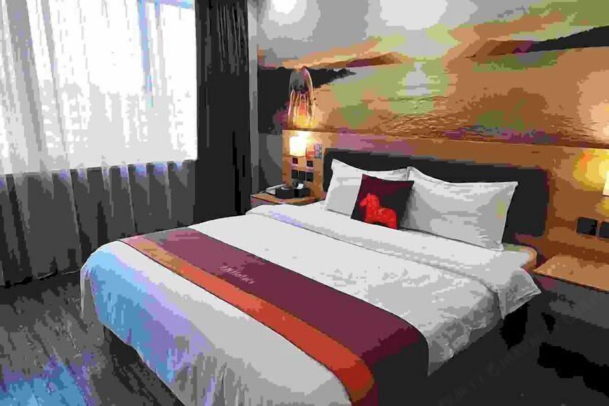 A hotel room with a bed, a nightstand, a lamp, and a painting on the wall.
