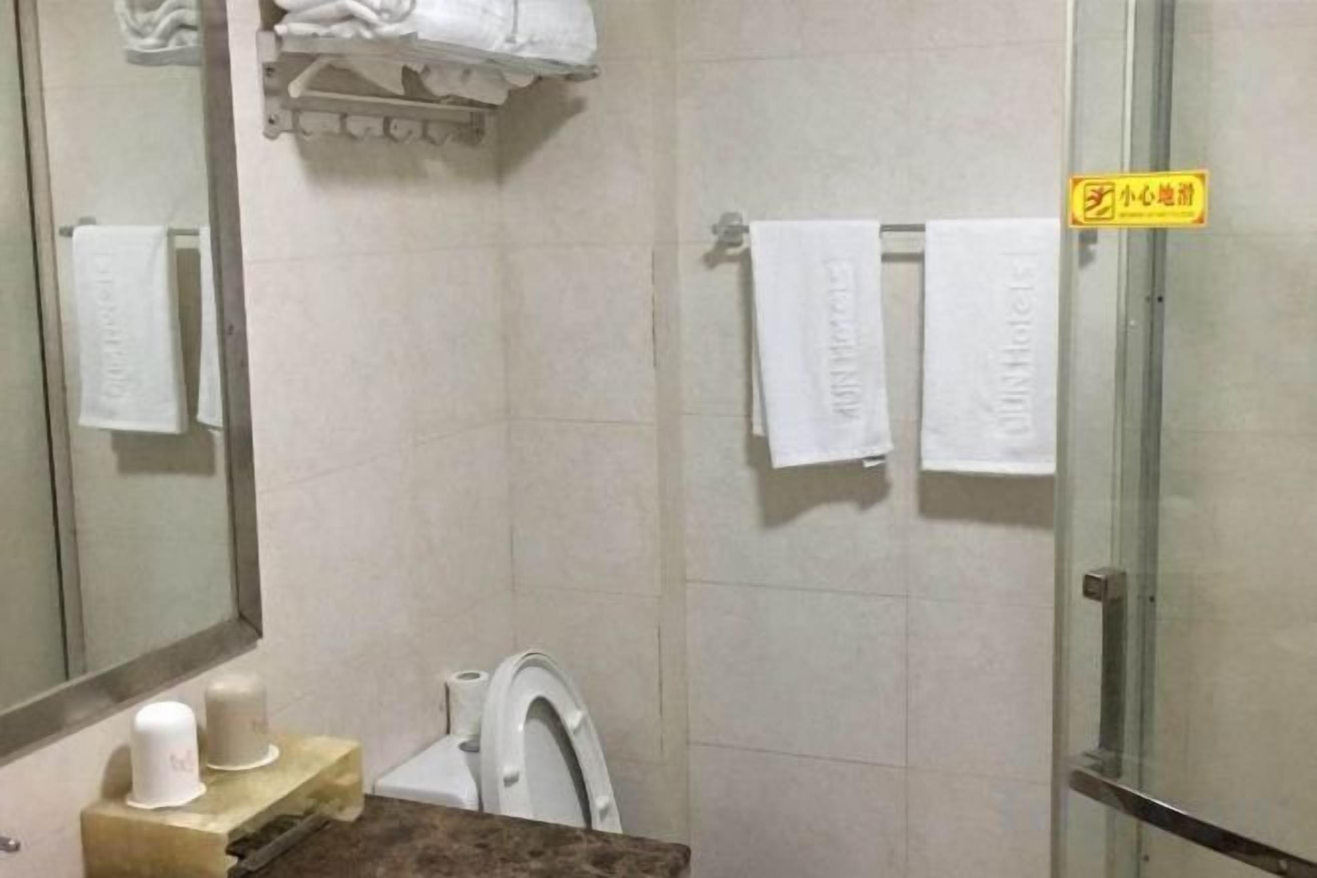 Ein Badezimmer mit Duschabtür aus Glas, Toilette und Handtuchhalter mit Handtüchern.