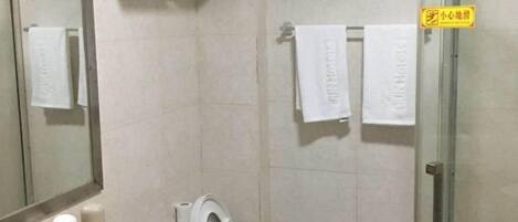 A bathroom with a glass shower door, a toilet, and a towel rack with towels.