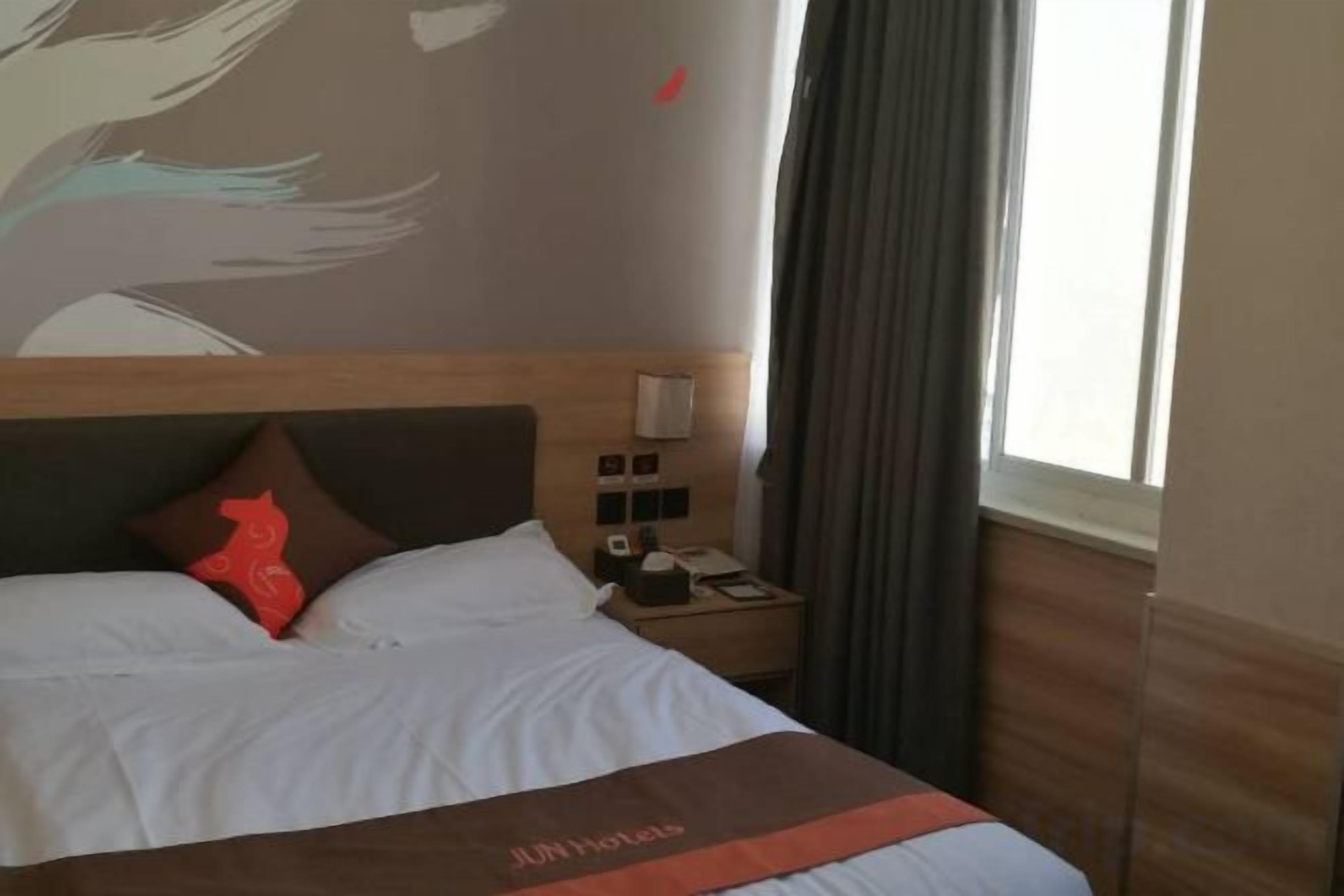 Une chambre d’hôtel avec un lit, une table de chevet, une horloge murale et une fenêtre avec des rideaux.