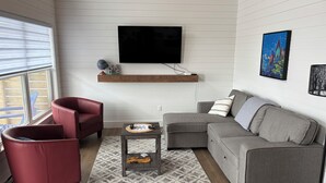 A living room with a grey sofa, red armchair, and a TV mounted on the wall. - Red Jellybean: great ocean views and sunsets close to town (Twillingate)