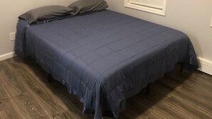 Un dormitorio con cama, ventana con persianas y piso de madera.