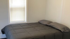 Un dormitorio con cama, ventana con persianas y suelo de madera.