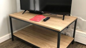 Un televisor negro sobre un mueble de madera con un control remoto y un folleto rojo.