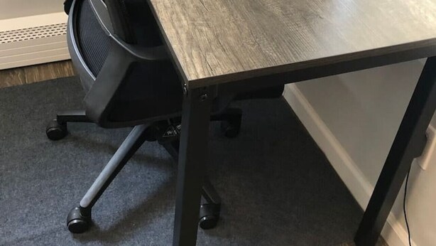 Oficina en esquina con una mesa de madera oscura, una silla de oficina negra y piso alfombrado.