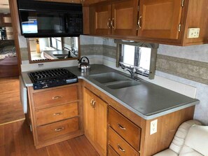 A compact kitchen with wooden cabinets, a built-in microwave, a stove, and a sink. - Unique private RV stay with full hookups, direct Manhattan bus 2 blocks away (Linden)