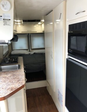 A compact RV interior with a kitchenette, a bed, and a microwave.