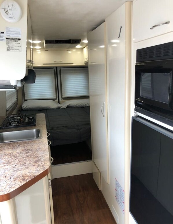 A compact RV interior with a kitchenette, a bed, and a microwave.