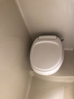 A white toilet in a bathroom with a plain wall and no visible amenities or features. - Cozy private camper with hookups, budget base for NYC, bus 2 blocks away (Linden)