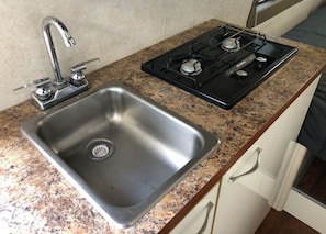 A kitchen with a stainless steel sink, a gas stove, and granite countertops. - Cozy private camper with hookups, budget base for NYC, bus 2 blocks away (Linden)
