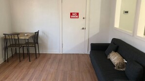 A room with a dining table and chairs, a black sofa, and a door with a 'NO SMOKING' sign.