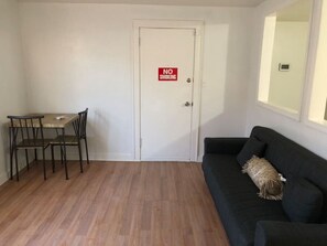 A room with a dining table and chairs, a black sofa, and a door with a 'NO SMOKING' sign.