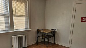 A room with a wooden floor, a table with four chairs, a radiator, and a door with a no smoking sign.