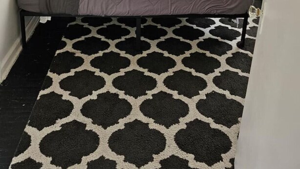 Un dormitorio con cama, estanterías empotradas, alfombra estampada y una puerta con picaporte dorado.