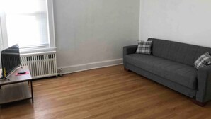 A room with a grey sofa, a small table with a TV and remote, and a radiator.