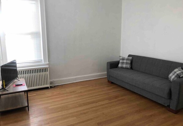 A room with a grey sofa, a small table with a TV and remote, and a radiator.