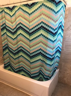 A bathroom with a white bathtub and a multicolored, zigzag patterned shower curtain.