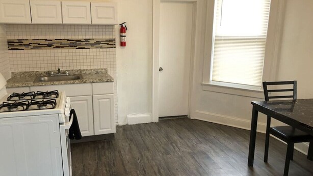 A kitchen with white cabinets, a gas stove, a tiled backsplash, and a dark wooden floor.