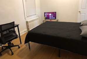 Ett sovrum med en säng, ett skrivbord och en datorskärm.
