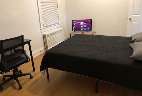 A bedroom with a bed, a desk, and a computer monitor.