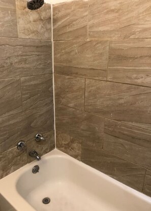 A bathroom with a bathtub, tiled walls, and a shower drain.